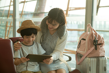年轻妈妈和儿子在机场候机厅看平板电脑图片