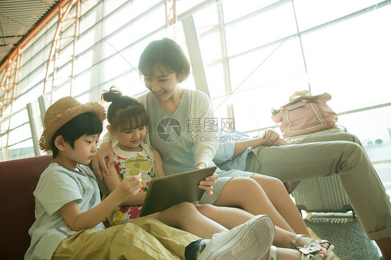 年轻妈妈和孩子们在机场候机厅看平板电脑图片
