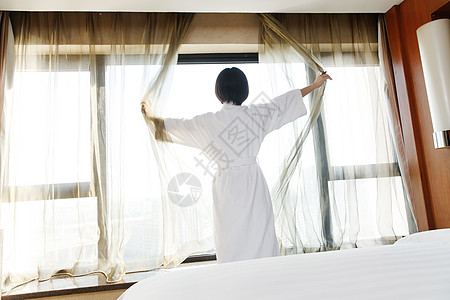 早晨开窗年轻女人在酒店房间里拉开窗帘背景