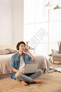 年轻的男青年坐在地板上使用笔记本电脑图片