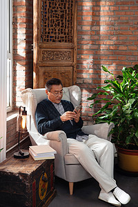 休闲的老年男人坐在沙发上玩手机图片