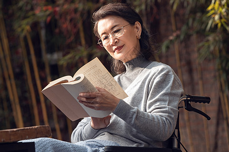 户外老年女人坐在轮椅上看书图片