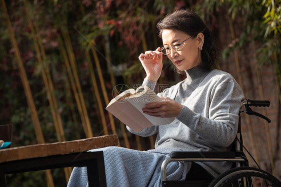 户外老年女人坐在轮椅上看书图片