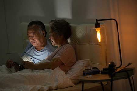 老年夫妇坐在床上用平板电脑看视频图片