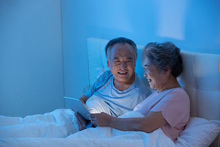 夜晚卧室老年夫妇坐在床上用平板电脑看视频背景