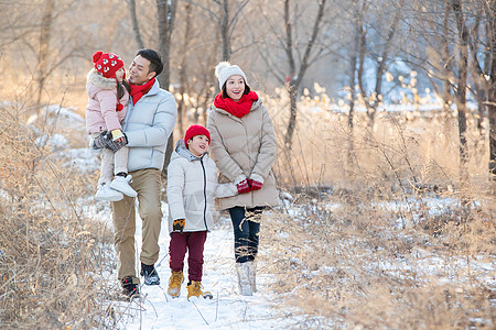 抱着木头男孩快乐家庭在雪地里散步背景