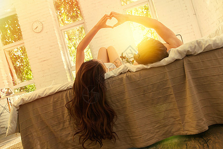 快乐的年轻情侣躺在床上做心形手势图片