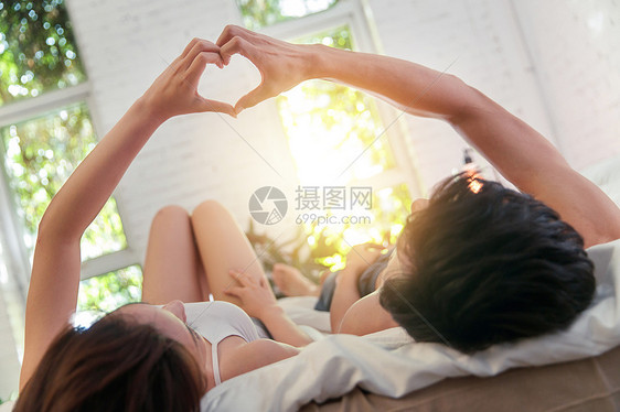 幸福的年轻伴侣躺在床上做心形手势图片