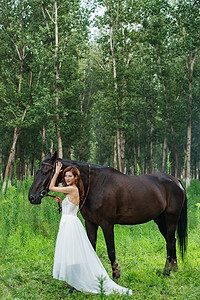 草地上穿婚纱的漂亮女人牵着马图片