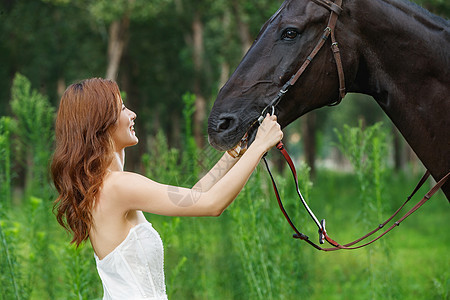 草丛中漂亮的青年女人牵着马图片
