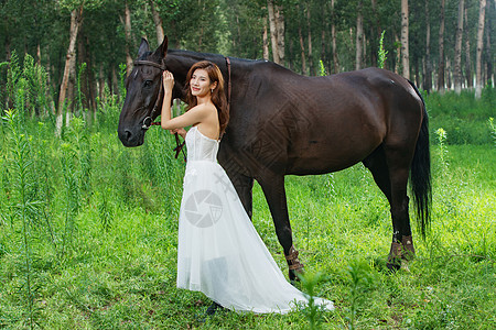 草地上漂亮的青年女人牵着马图片
