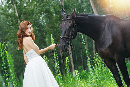 树林中牵着马的青年女人回眸一笑图片