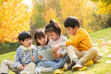 四个小朋友坐在草地上看平板电脑图片