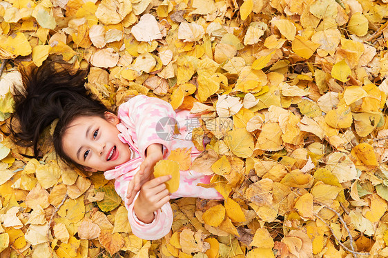 快乐的小女孩躺在落叶上玩耍图片