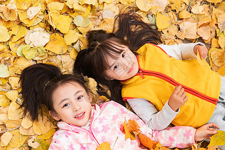两个小女孩躺在落叶上玩耍图片