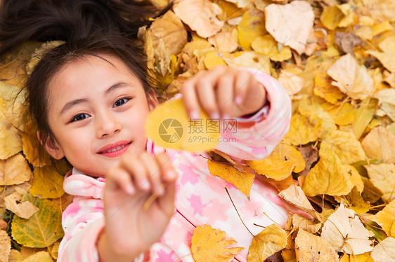 快乐的小女孩躺在落叶上玩耍图片