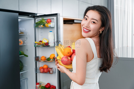 拿着水果的青年女人站在冰箱前图片