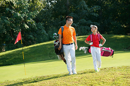 球场上教练和学生背着高尔夫球包行走图片