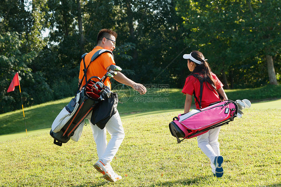 球场上教练和学生背着高尔夫球包行走图片