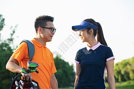 快乐的青年人背着高尔夫球包在球场对视图片