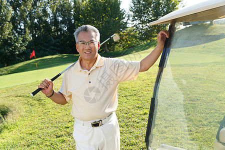 快乐的老年人扛着球杆站在高尔夫球车旁图片