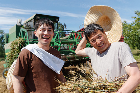 抱着小麦的男孩农田里实现机械化收割的农民背景