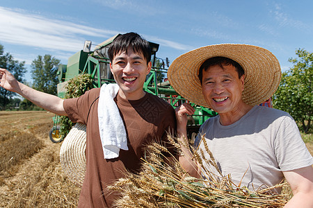 农民抱着麦穗农田里实现机械化收割的农民背景