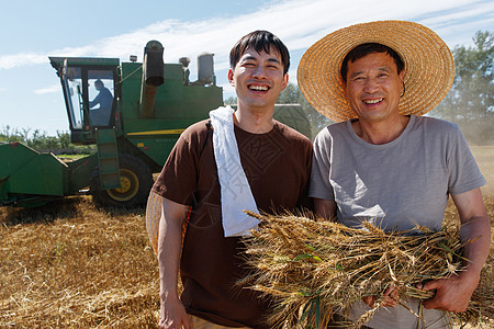 抱着小麦的男孩农田里实现机械化收割的农民背景