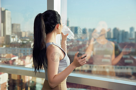 运动饮料健身后站在窗边喝水的女性背景