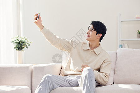 坐在客厅休息的年轻人使用手机自拍图片