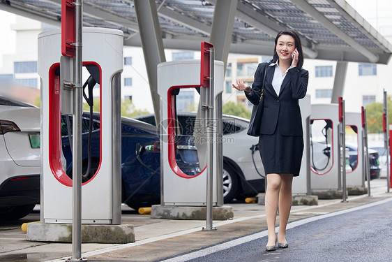 新能源汽车充电桩旁打电话的商务女性图片