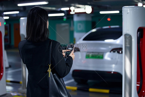 使用手机操作新能源汽车的女性背影图片