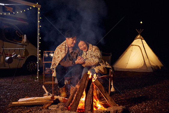 年轻情侣户外露营夜晚篝火取暖图片