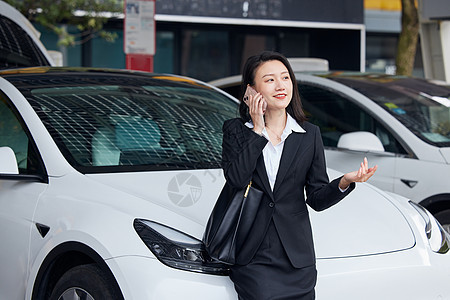 靠在新能源汽车旁打电话的商务女性图片