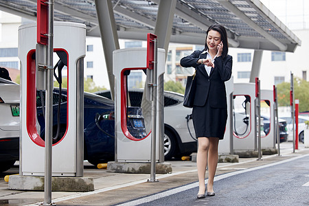 充电汽车新能源充电桩旁通话的商务女性背景