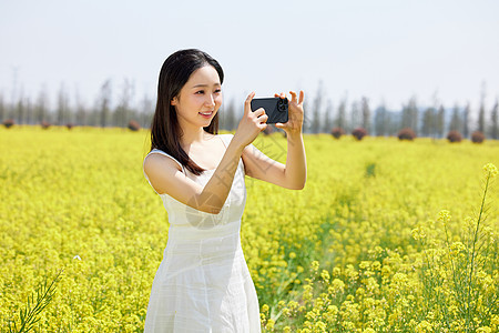 使用手机拍油菜花海美景的女性图片