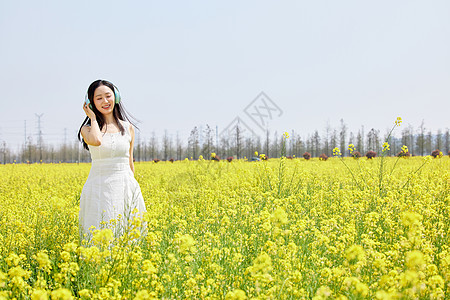 女性在油菜花海戴着耳机听歌高清图片