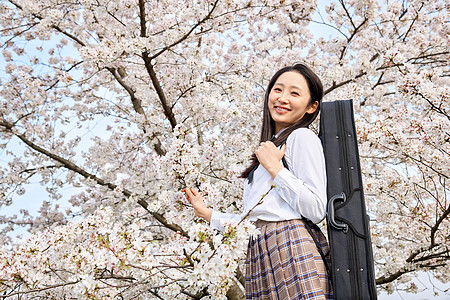 樱花树下背着乐器包的女性高中生图片