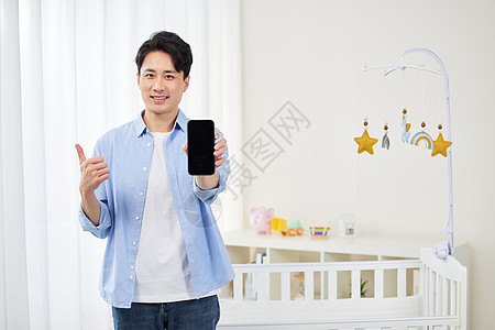年轻奶爸在婴儿房拿手机点赞背景图片