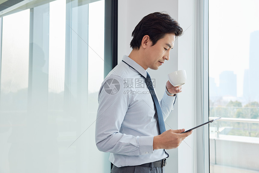 站在窗前喝咖啡办公的商务男士图片