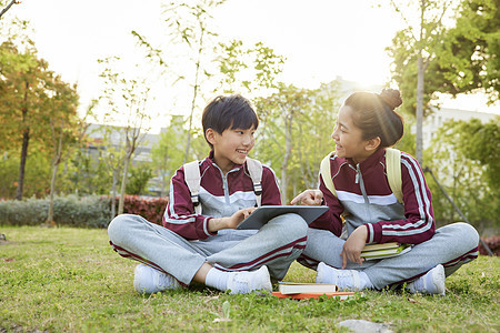 坐草地上的小学生使用平板电脑学习图片