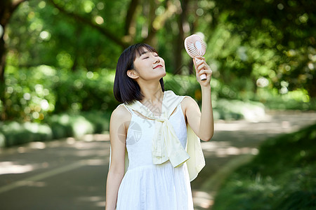 户外手拿便携风扇吹风的少女高清图片