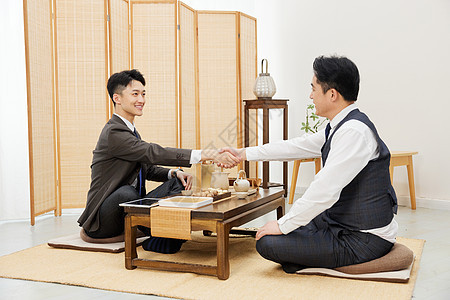 茶桌上生意合作的俩人握手图片