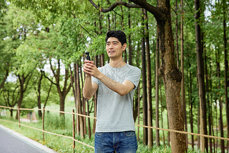手持手机拍照男性在公园手持录像设备背景