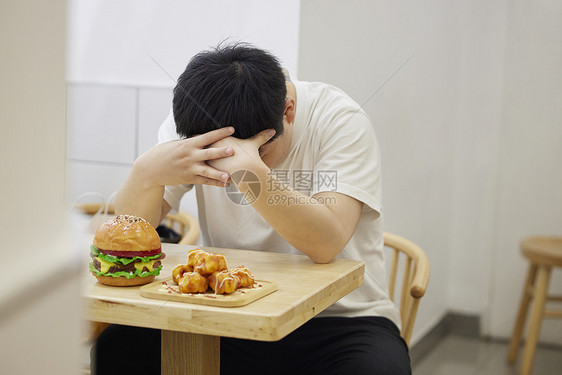 餐厅里肥胖的人对着高热量食物难过图片