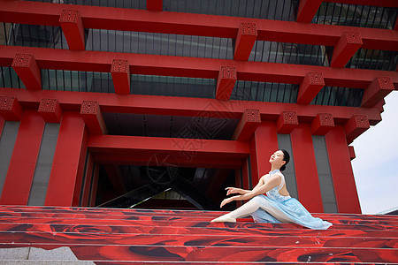 红色建筑前坐着的芭蕾舞者图片