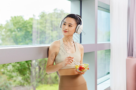戴耳机吃色拉休息的运动美女背景图片