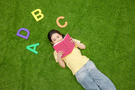 小女孩躺在草地上看书学习图片