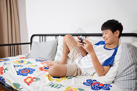 开心地在沙发上玩手机的男孩高清图片