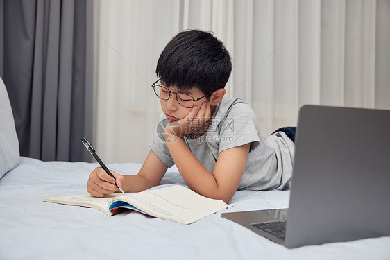 在床上补作业的男孩图片